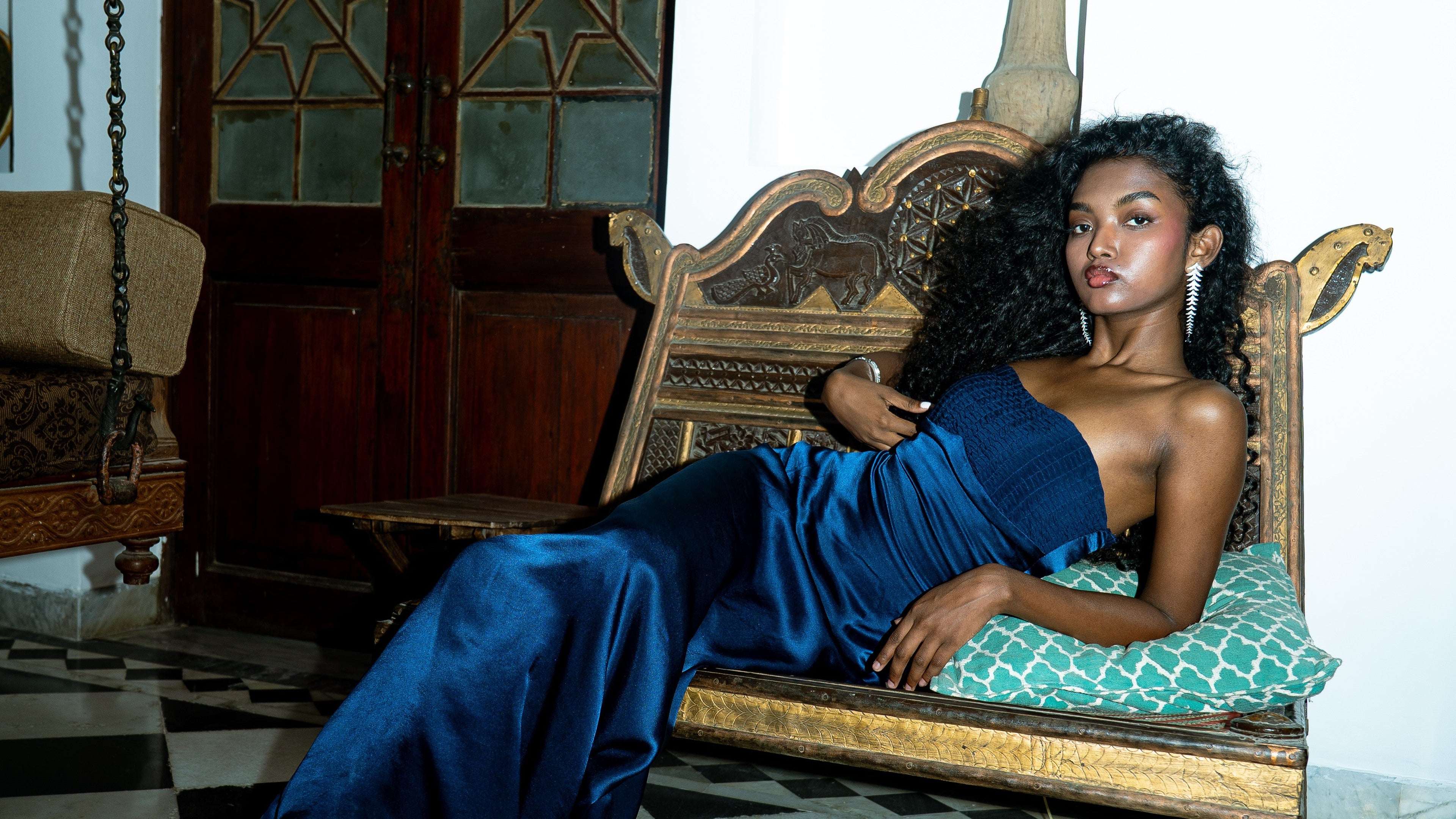Woman in a blue dress sitting on a wooden bench in a room with a checkered floor.
